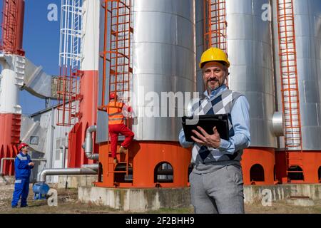 Portrait of Business Person with Two Workers in Personal Protective Equipment at Maintenance Work in District Heating Power Plant. Teamwork Concept. Stock Photo