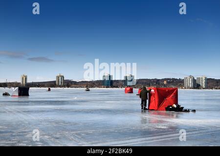 Barrie, Ontario, Canada - March 7, 2021: Ice fishing tents on frozen Kempenfelt Bay of Lake Simcoe in winter with highrise condos of Barrie Stock Photo