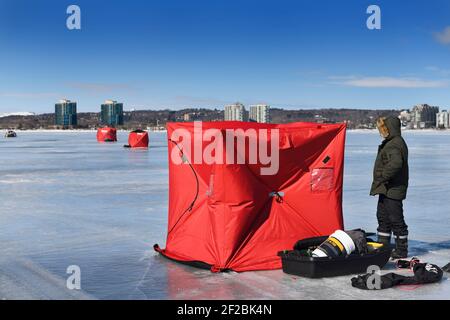 Barrie, Ontario, Canada - March 7, 2021: Fisherman erecting a red ice fishing tent on frozen Kempenfelt Bay of Lake Simcoe in winter Stock Photo