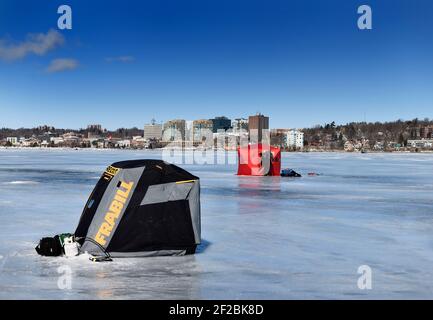 Barrie, Ontario, Canada - March 7, 2021: Fisherman exiting a red ice fishing tent on frozen Kempenfelt Bay of Lake Simcoe in winter with Barrie citysc Stock Photo
