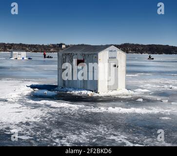 Ice fishing shacks on frozen Kempenfelt Bay of Lake Simcoe in winter with fishermen fishing and hauling a sled Stock Photo