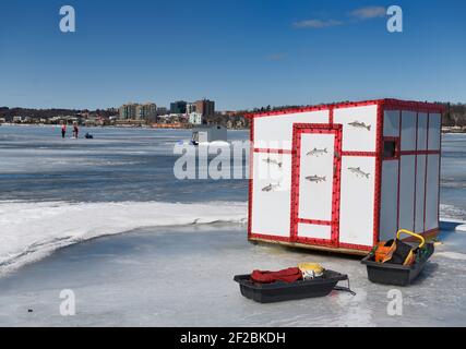 Ice fishing shack with sleds and fishermen drilling hole on frozen Kempenfelt Bay of Lake Simcoe at Barrie Canada Stock Photo