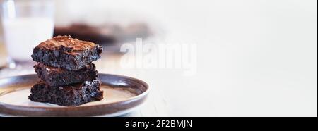 Banner of fresh made homemade fudgy brownies stacked on a saucer over a white rustic wooden table. Shallow depth of field with blurred background. Stock Photo