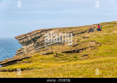 Birdwatchers sitting on top of sea cliffs at Brough of Birsay, Orkney. Stock Photo