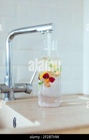 Filling a clear glass carafe with tap water. Water is infused with berries, mint and lemon Stock Photo