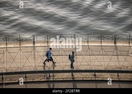 Prague, Czech republic - February 24, 2021. Two people walk on the pathway by Moldau river in sunset - one with mask, second without protection Stock Photo