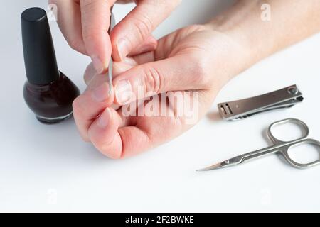 Woman hands doing manicure. Female hands, holding nail file, with nail polish, scissors and nail clippers on white background. Stock Photo