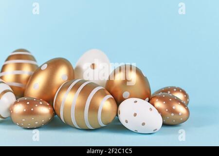 Golden and white Easter eggs painted with simple dots and stripes on blue background Stock Photo
