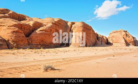 4wd vehicle tire tracks in sand desert, large rocky massif distance, clear blue sky above - typical scenery of Wadi Rum, Jordan Stock Photo