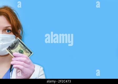 A blue uniform doctor is upset about money problems, blue background. A nurse in a medical hat and mask holds a torn one hundred dollar bill, copy spa Stock Photo