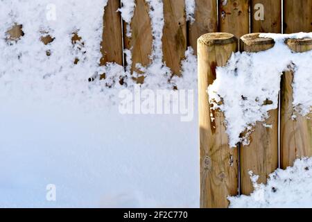 A fence made from round wooden stakes plastered and covered in deep fresh snow. Stock Photo