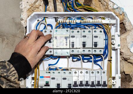 The electrician turns off the input automatic toggle switch of the electrical panel built into the wall of the house. Electricity control device. Stock Photo
