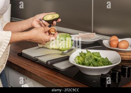 Side view of anonymous crop woman preparing avocado for healthy salad while cooking lunch at counter at home Stock Photo