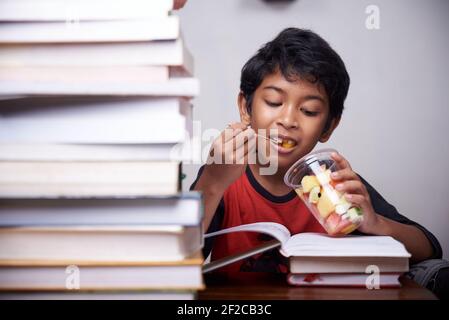 Little boy eating mixed fruit after study at home Stock Photo