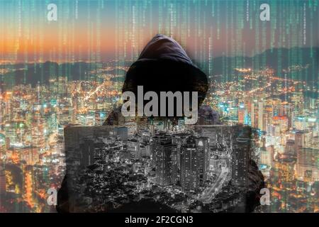 silhouette of a man in a hood working as a hacker at the computer in the dark room at night, hacking the system and laundring secret information. Stock Photo