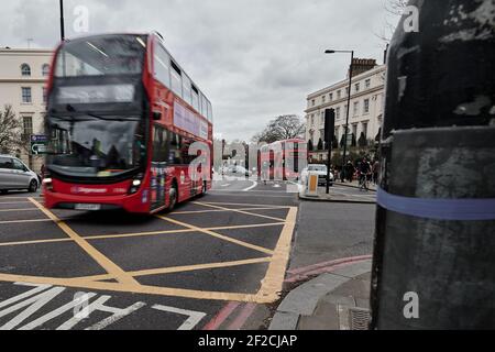 LondonUK - 6 Mar 2021: Motion Blurred image of modern red london double decker bus passing through a busy traffic junction over yellow hashed box Stock Photo