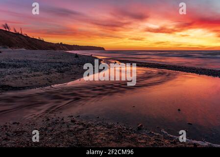 sunset on the seashore and the source of the river with sunset-colored colors and a beautiful sky with clouds hiding the sun Stock Photo