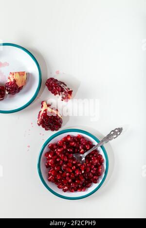 Fresh pomegranate seeds in plate with pomegranate slices on white table. Stock Photo