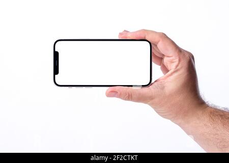 Antalya, Turkey - March 07, 2021: Hand holding black smartphone iPhone 12 with white screen. Isolated on white background. Mobile phone frameless desi Stock Photo