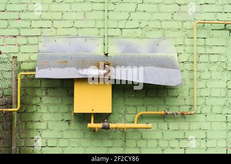 Old yellow pipeline and box covered with corroded tin sheet on green brick wall horizontal Stock Photo