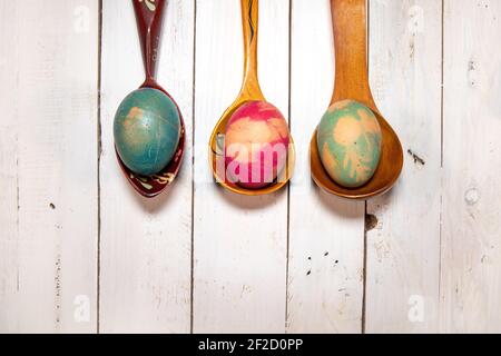 Flat lay with Easter eggs and spoons. Three wooden spoons with natural colored eggs on a white shabby chic background. Stock Photo