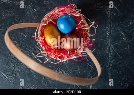 Homemade multicolored painted Easter eggs on colorful straw in a wicker basket on a dark background Stock Photo