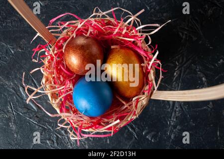 Homemade multicolored painted Easter eggs on colorful straw in a wicker basket on a dark background Stock Photo