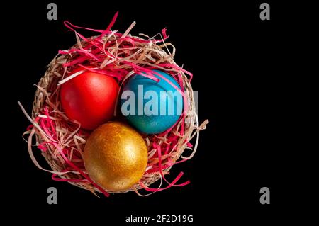 Homemade multicolored painted Easter eggs on multicolored straw in a wicker basket on a dark background, isolation Stock Photo