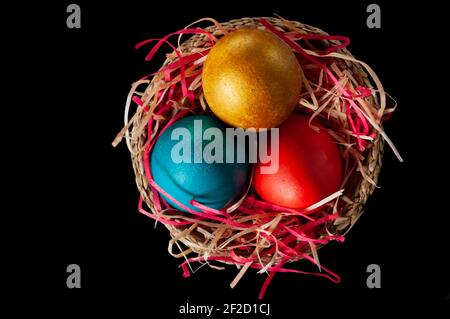 Homemade multicolored painted Easter eggs on multicolored straw in a wicker basket on a dark background, isolation Stock Photo
