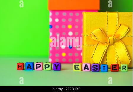 Happy Easter multicolored words written with wooden alphabet letters on a bright green background. Gift boxes in the background. Greeting card for Chr Stock Photo