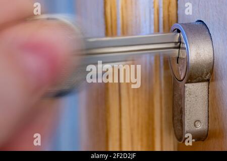 A hand puts the key in the keyhole. The key inserted in a wooden door lock, close up view. Stock Photo