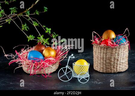 Homemade multicolored painted Easter eggs on colorful straw in wicker baskets and in stands on a dark background, Easter decoration Stock Photo