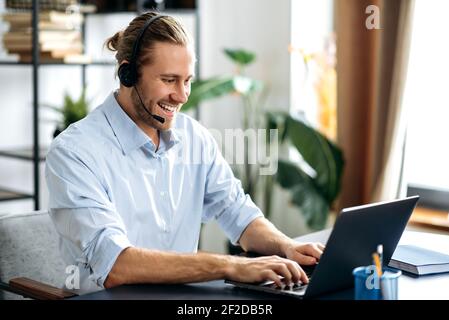 Confident friendly modern male manager or call center worker in headset is looks at the laptop screen, having online business meeting. Successful employee talking online with colleagues uses laptop Stock Photo