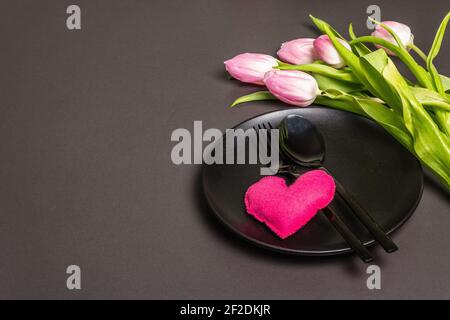Festive creative black table setting with tulips and felt heart on dark background. Valentine's Day, Wedding, Birthday, Women's, and Mother's Day. Fla Stock Photo
