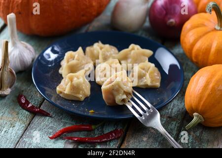 Traditional Uzbek dish. Manti, steam dumplings on navy blue plate decorated with raw pumpkins, onions and chili peppers on blue rustic background clos Stock Photo