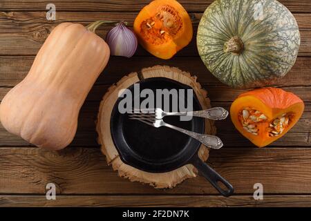 Flatlay of raw pumpkins and empty cast iron pan on rustic wooden background overhead view Stock Photo