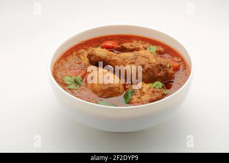 Chicken curry or masala , spicy reddish chicken leg piece dish garnished with coriander leaf and  fresh green chilli which is arranged in a white cera