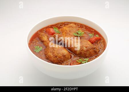 Chicken curry or masala , spicy reddish chicken leg piece dish garnished with coriander leaf and  fresh green chilli which is arranged in a white cera