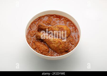 Chicken curry or masala , spicy reddish chicken leg piece dish garnished with coriander leaf and  fresh green chilli which is arranged in a white cera Stock Photo
