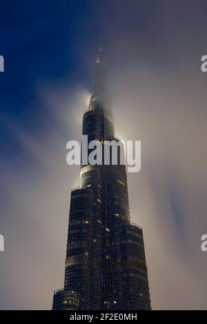Burj Khalifa building at night with the top covered by low cloud. Skyscraper in Dubai, United Arab Emirates. Highrise top behind clouds. Stock Photo