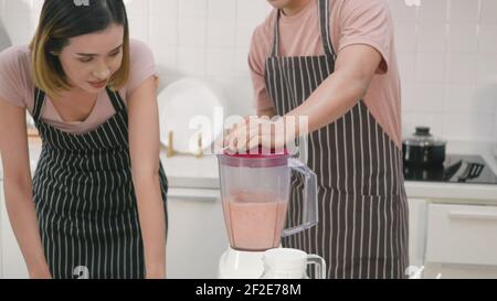 Happy young family couple husband and wife making fresh apple smoothie in kitchen together. The man and woman help each blender the apples with a juic Stock Photo