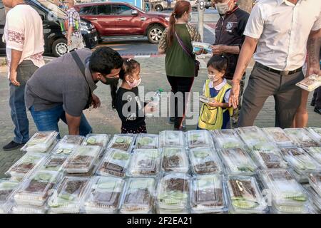 Asian Indian child helping by handing out free food and drink to Thai counterpart effected by the economical life changes of the Covid 19 pandemic. Stock Photo