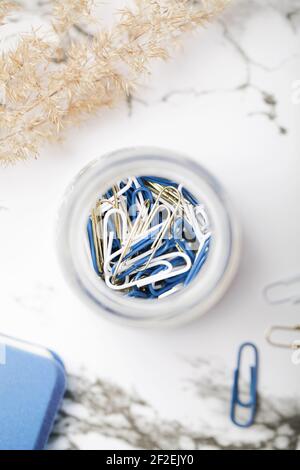 paper clips in glass jar with pampas grass and notepad on white background. working space. office stationery concept. selective focus.  Stock Photo