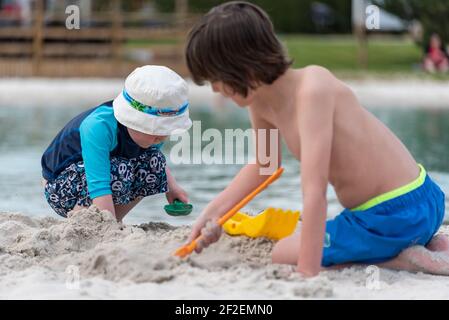 Two young boys playing in the sand by a lake. Stock Photo