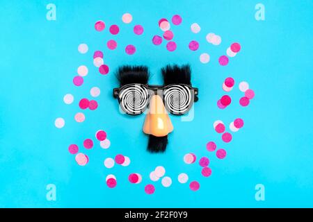 funny face - fake eyeglasses, nose and mustache, confetti, sequins on blue background Happy fools day concept 1st April party Holiday card Stock Photo