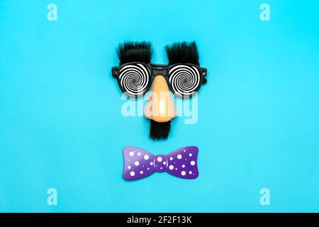 funny face - fake eyeglasses, nose and mustache, confetti, sequins on blue background Happy fools day concept 1st April party Holiday card Stock Photo