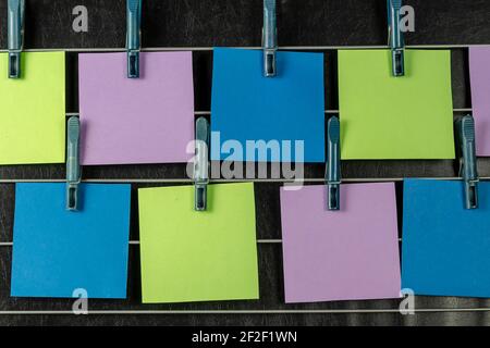 The paper sticky notes hanging from clothespins. Set of multicolored blank square stickers on black background. No people. Stock Photo
