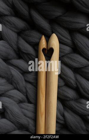 Two wooden knitting needles lying on gray merino wool, in the form of a heart Stock Photo