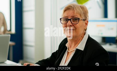 Portrait of senior businesswoman looking at camera sitting in brainstorming room, preparing for meeting with partners. Manager working in professional start up financial business ready for conference Stock Photo