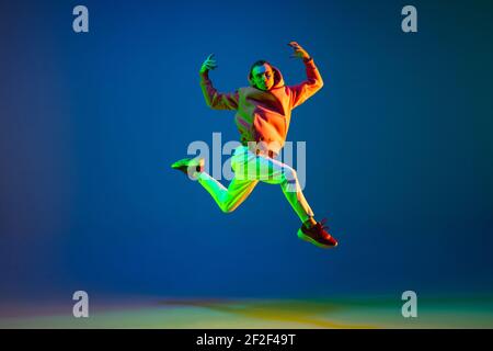 Young male dancer jumping isolated over on blue background in neon light Stock Photo